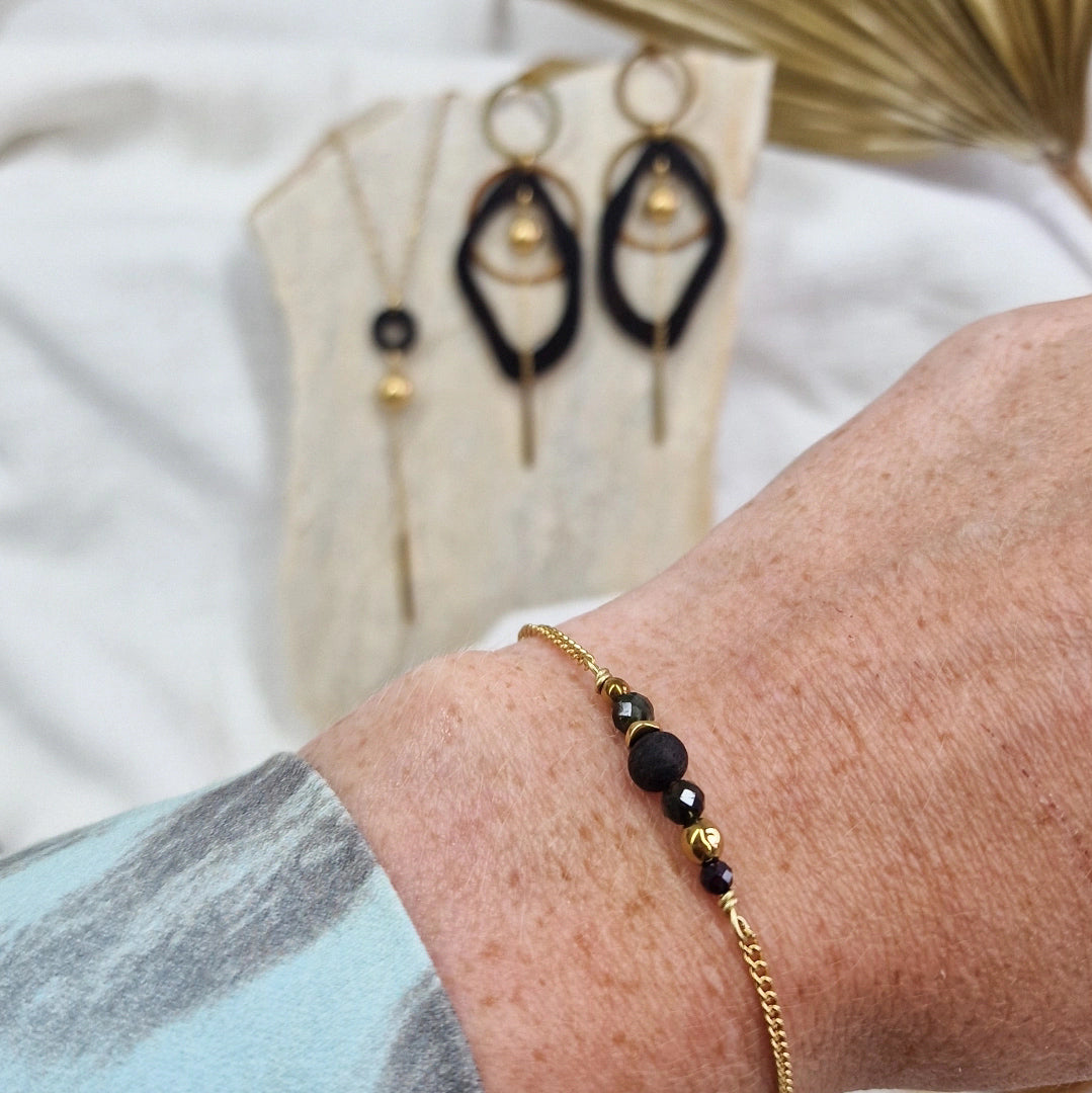 Armband aus Räuchereiche mit Holzperlen und goldfarbener Kette am Handgelenk getragen, im Hintergrund passende Ohrringe und Halskette