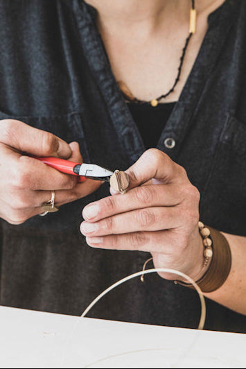 Detailaufnahme zweier Hände die eine Zange und einen Ring in der Hand halten, weil sie ihn gerade gefertigt haben. Im Vordergrund ein Stück Draht