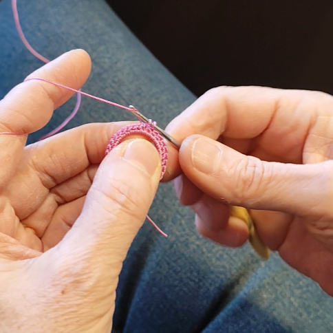 Hände beim Häkeln eines Rings aus rosa Garn für handgefertigte Ohrringe