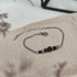 Armband aus Räuchereiche mit Holzperlen und silberfarbener Kette auf einem braunen Webare-Kissen, im Hintergrund eine Ecke Glaskasten und Strauch im Vordergrund