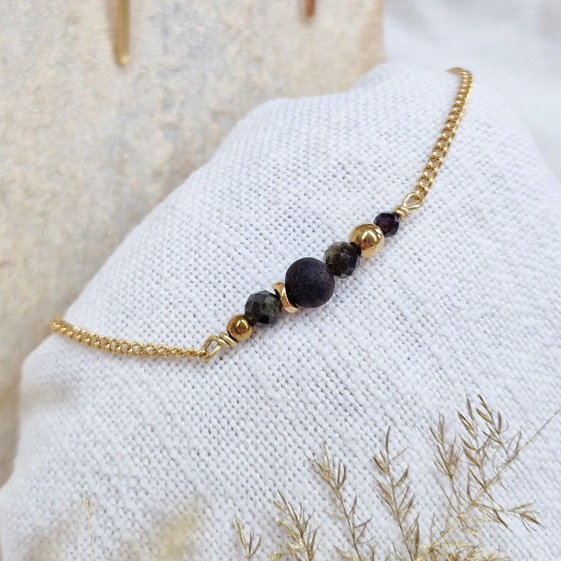 Armband aus Räuchereiche mit Holzperlen und goldener Kette auf einem weißen Webare-Kissen, im Hintergrund ein heller Stein
