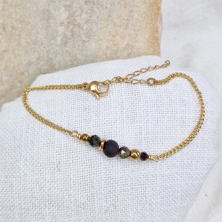 Armband aus Räuchereiche mit Holzperlen und goldener Kette auf einem weißen Webare-Kissen, im Hintergrund ein heller Stein